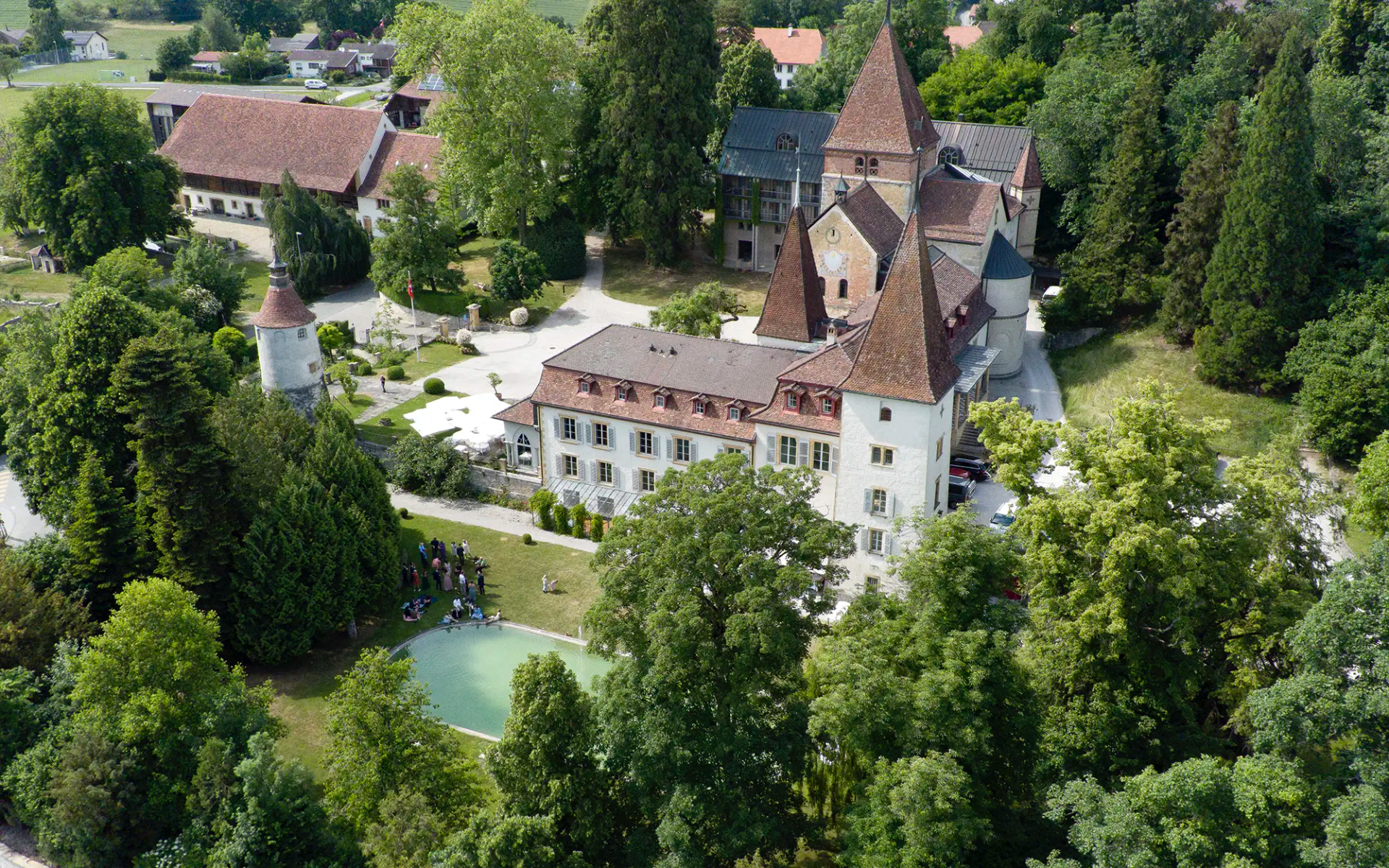 Luftaufnahme des Schloss Münchenwiler mit Schlosspark und Hochzeitsgästen während einer Hochzeitsreportage