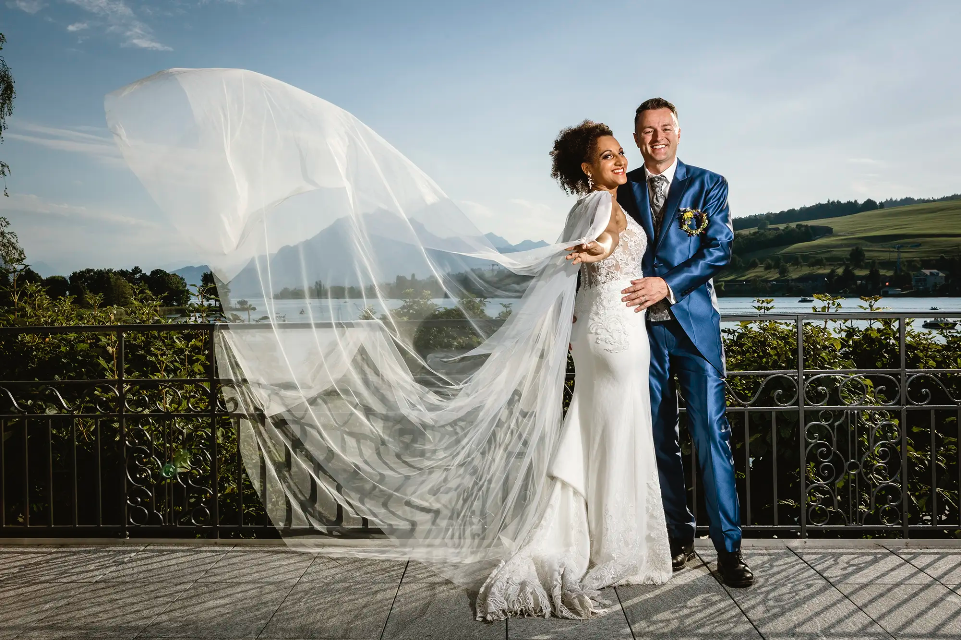 Cécile und Michael beim Paarshooting auf dem Balkon des Hotel Seehof in Küssnacht mit wehendem Schleier und Blick auf den Vierwaldstättersee.