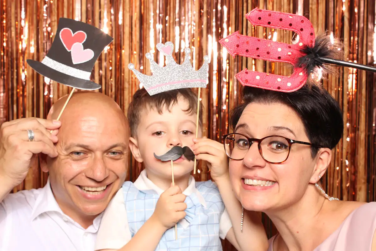 Fröhliche Gäste mit Requisiten an der Selfiebox bei der Hochzeit im Hof Landschi
