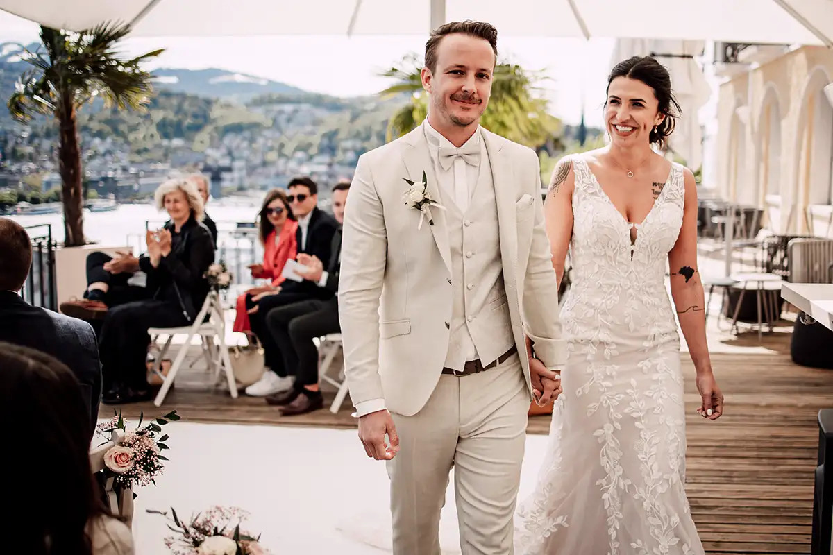 Nando und Patricia nach der freien Trauung im Hotel Montana Luzern mit Gaesten im Hintergrund