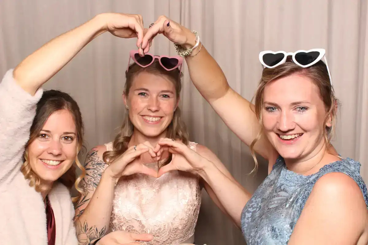 Drei Hochzeitsgäste formen vor der Selfiebox im Biohof Zug gemeinsam ein Herz.