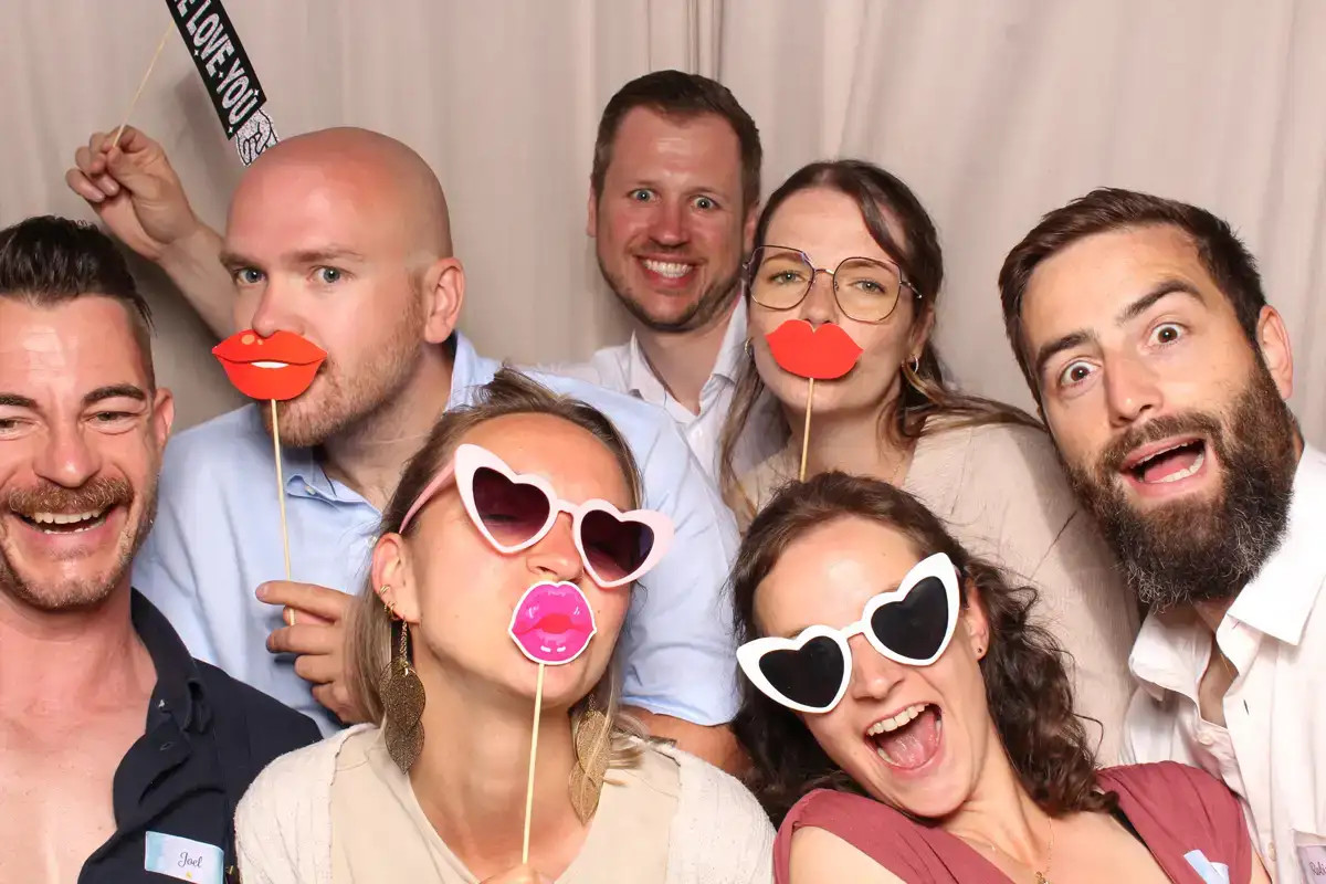 Eine ausgelassene Gästegruppe feiert mit farbigen Requisiten vor der Selfiebox.